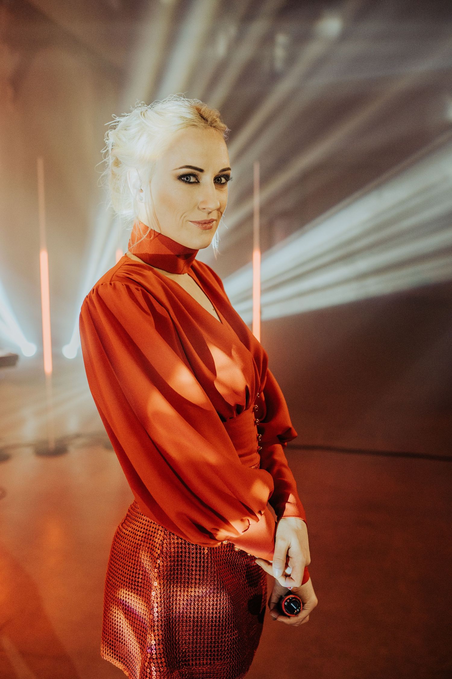 Performer in a striking red outfit performing on stage with dramatic lighting and fog effects.