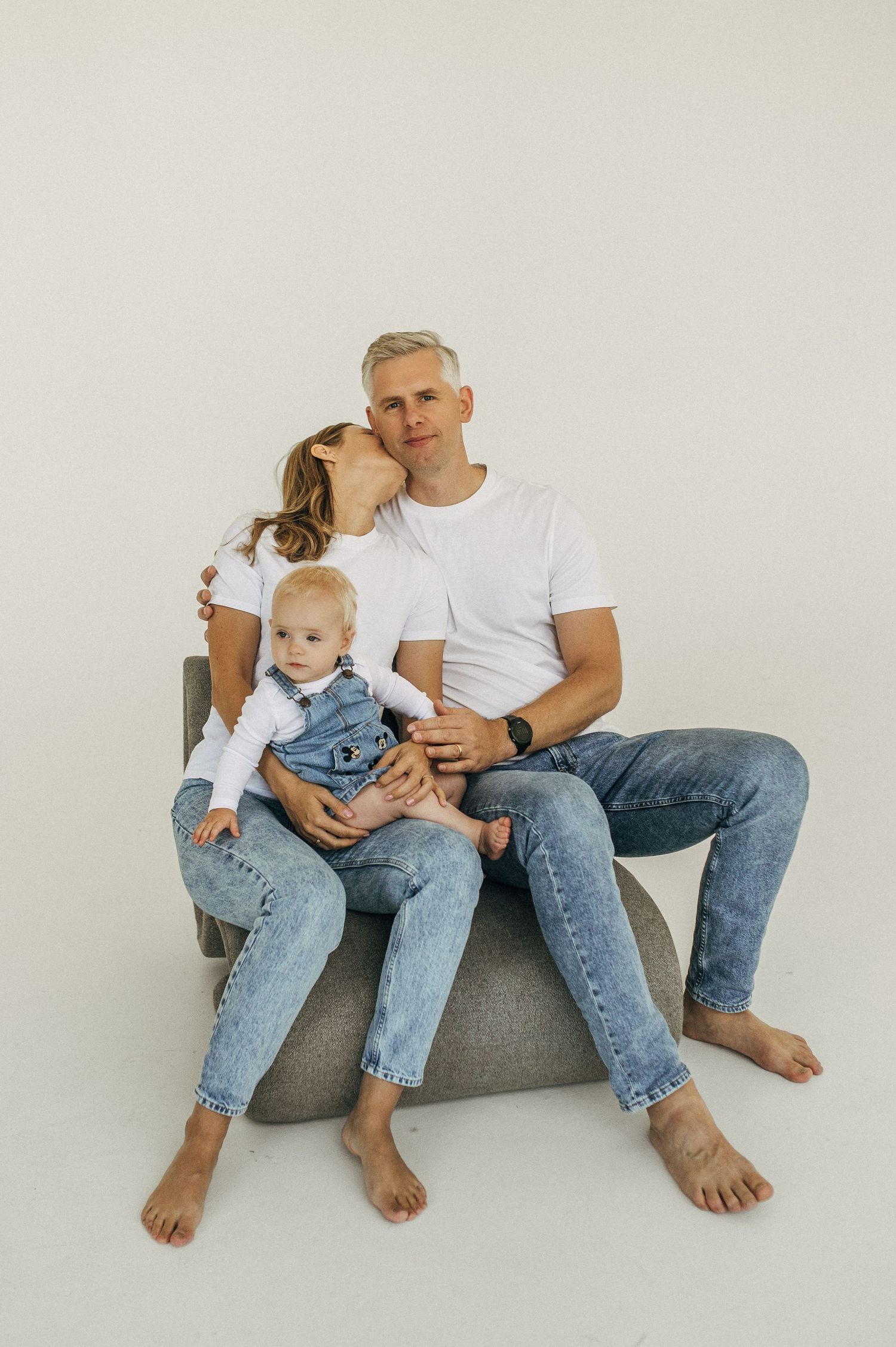Family sitting together on a gray couch wearing casual denim and white t-shirts.