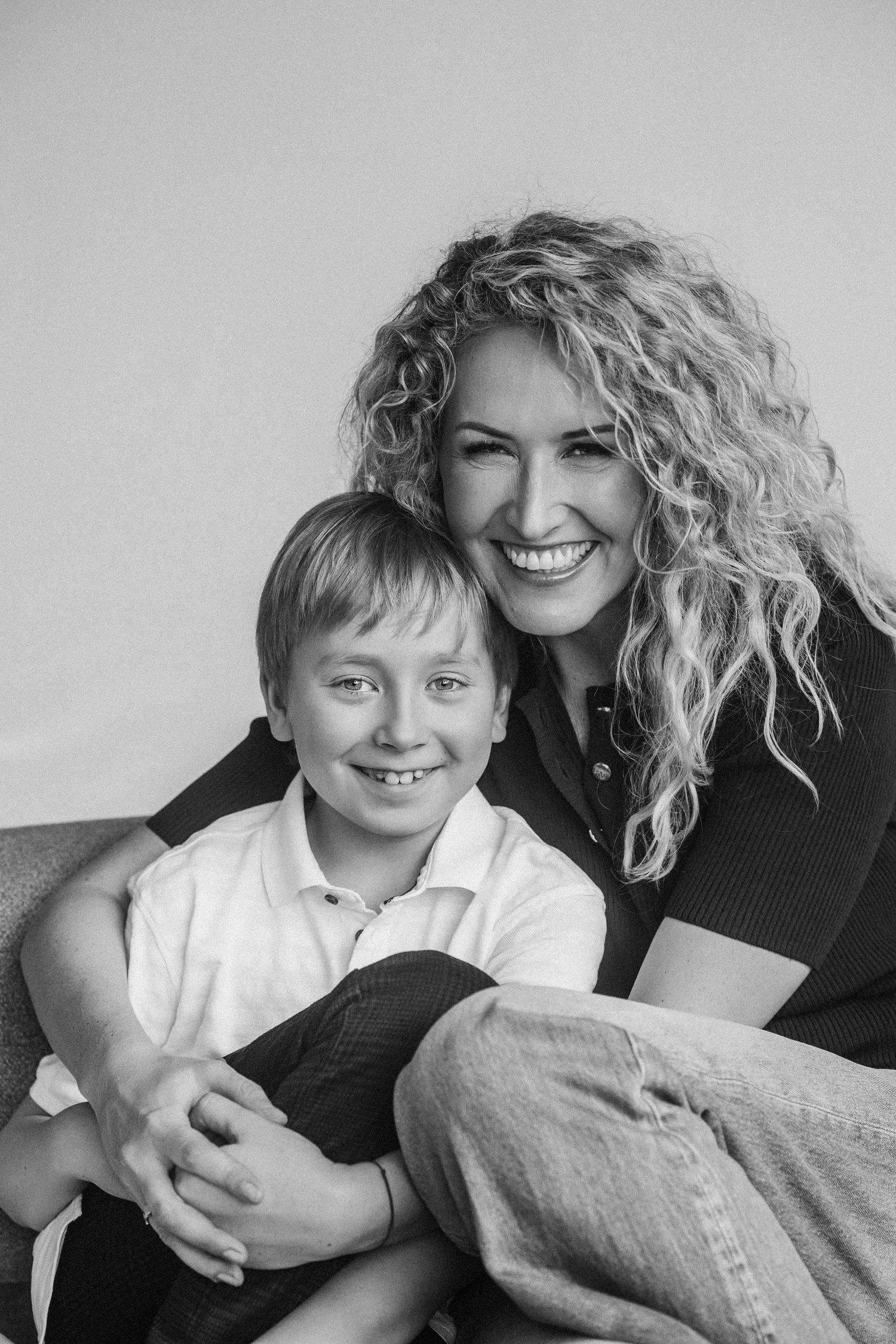 Black and white portrait of a smiling woman with curly hair hugging a young boy, both looking at the camera.