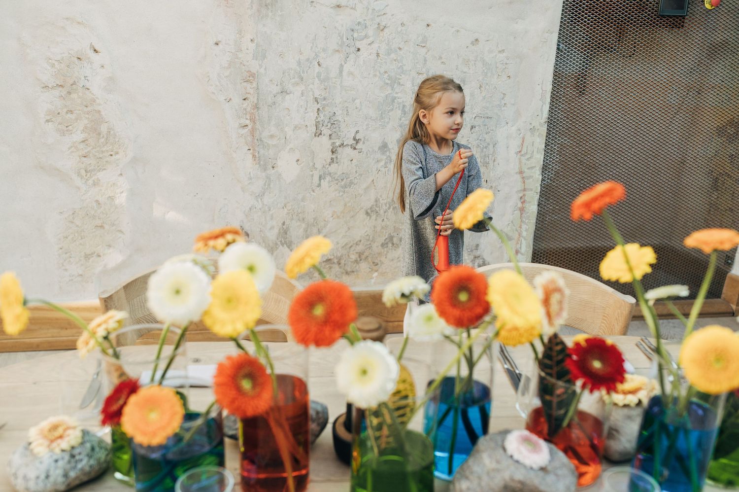 Young girl standing among colorful gerbera daisies in glass vases at a flower market.
