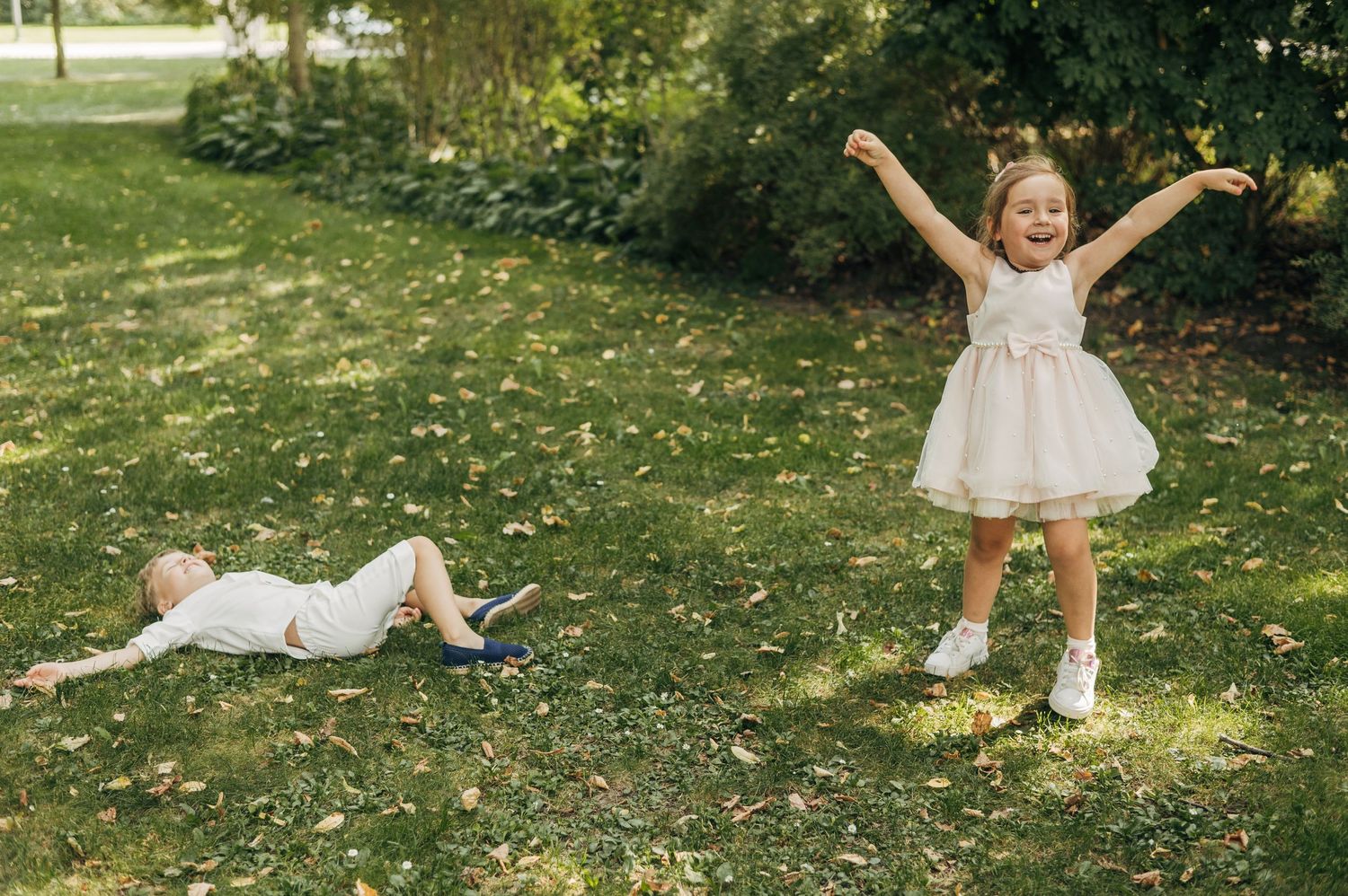 Child in white dress plays energetically on grass spreading arms wide with pure joy.