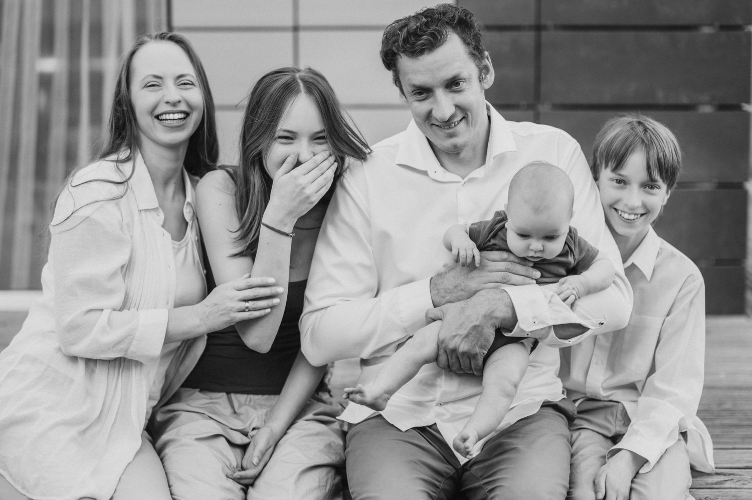 Black and white photo of a family sharing a candid moment of laughter together on a bench.