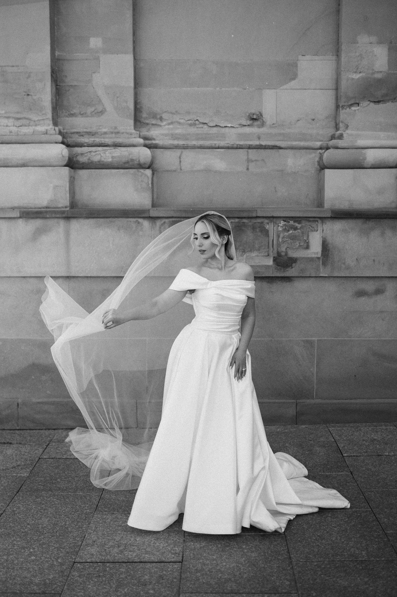 Black and white series of a bride in flowing white dress creating dramatic movement against stone architecture.
