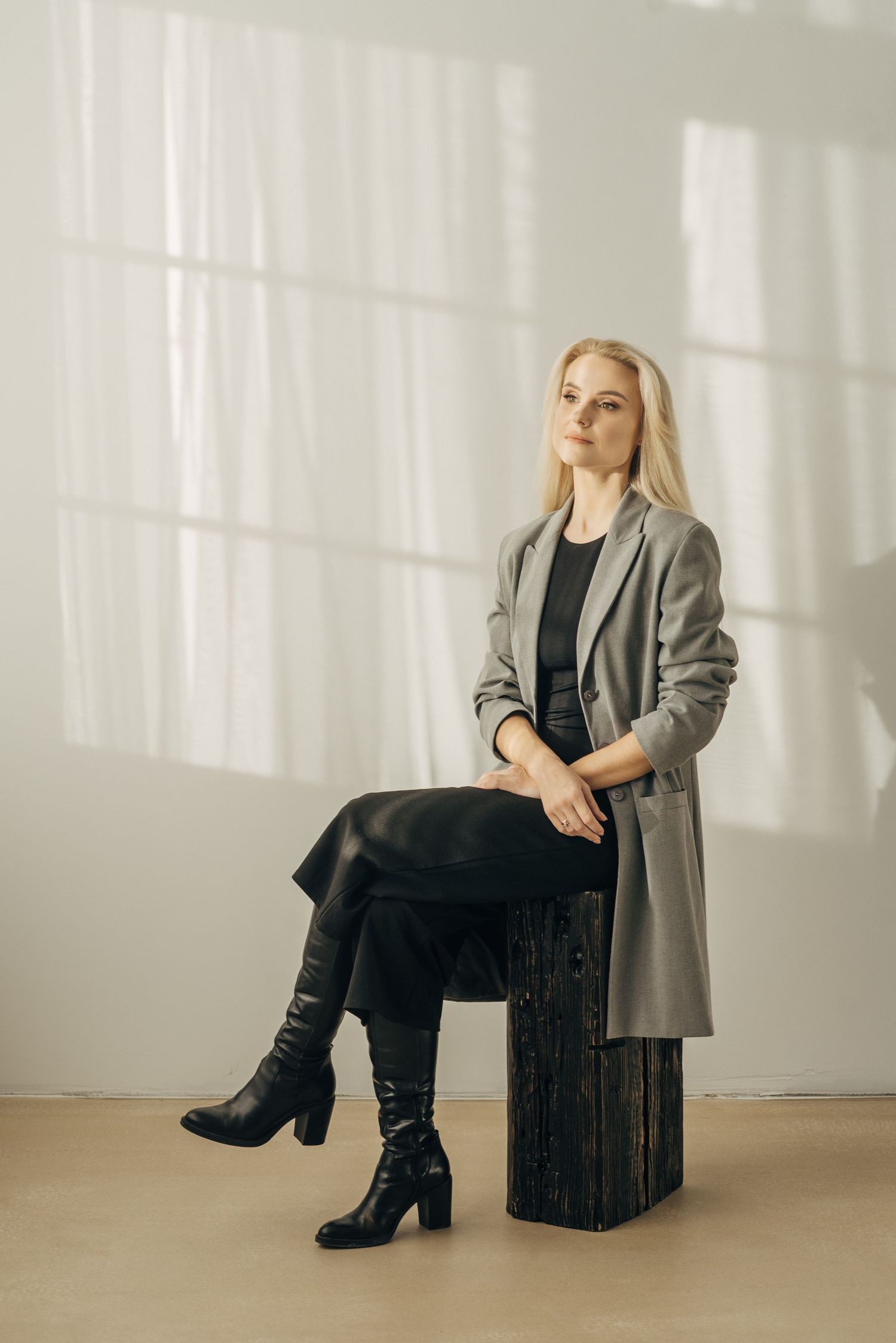 Fashion editorial shots showing grey blazer and boots while seated on dark wooden box.