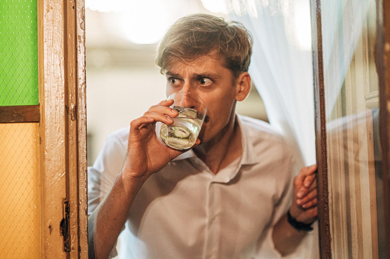 Person in white shirt sits at table drinking from glass in sequence of three connected photos.