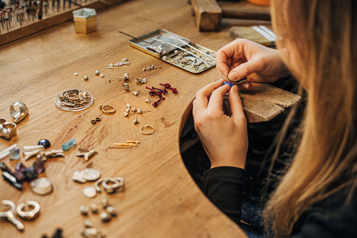 Close-up view of hands working on delicate jewelry pieces on a wooden surface.