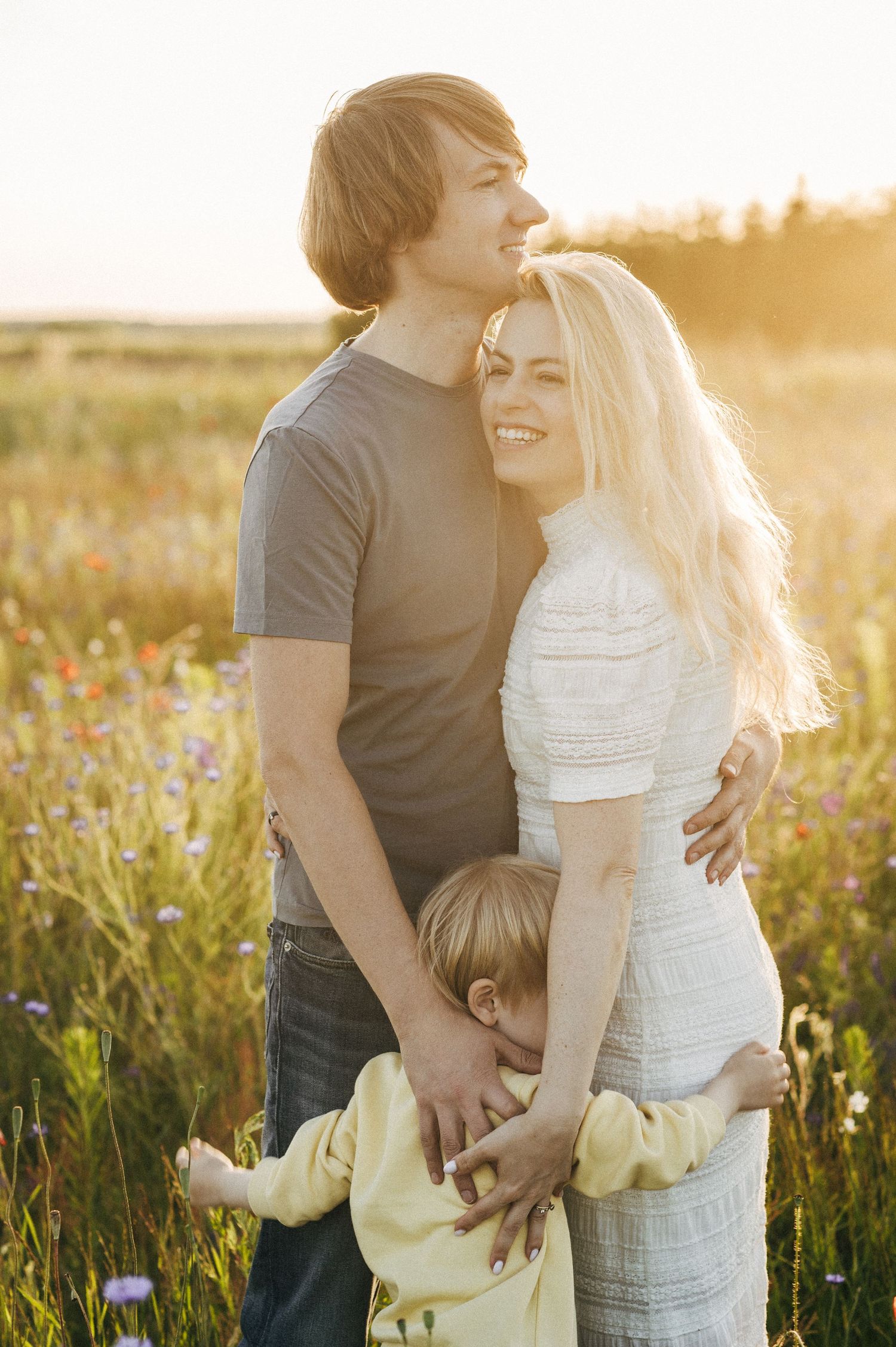 A couple embracing in a sunlit meadow with golden light streaming through the flowers.