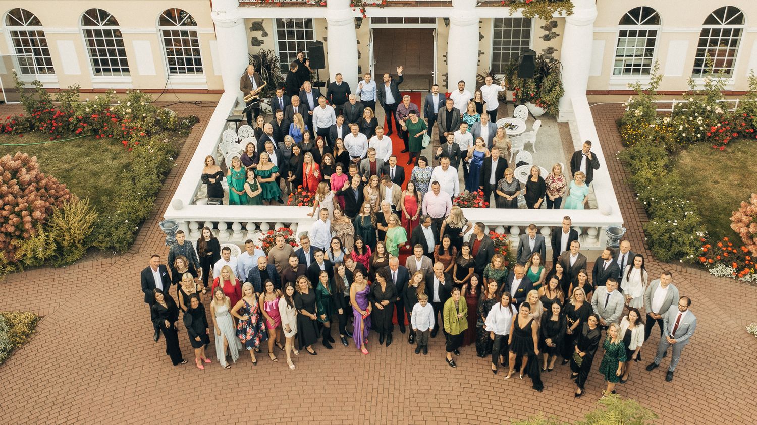 Large group photo of conference attendees gathered outside a building with arched windows.