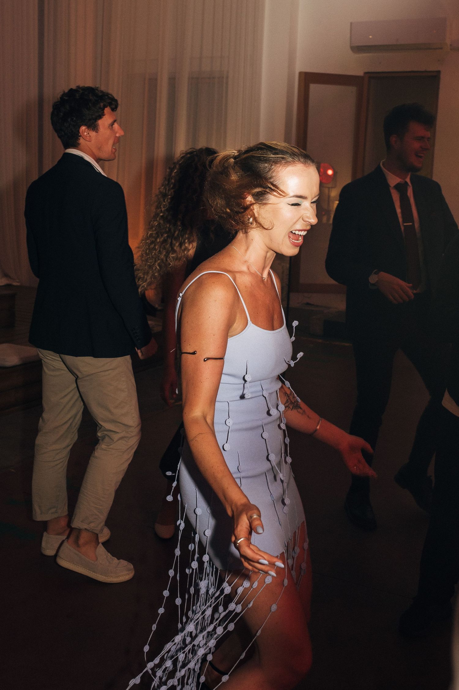 Woman in light blue dress laughing and dancing joyfully at an elegant evening wedding reception.