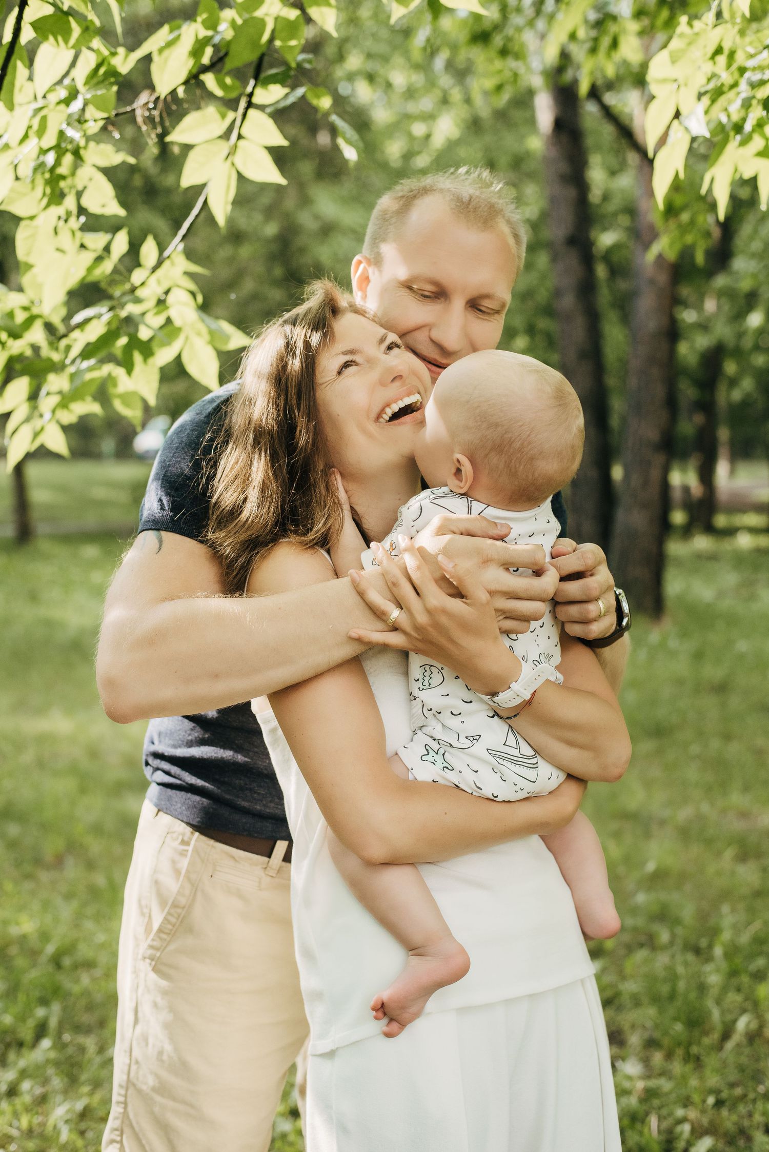 A tender family moment captured in a sunlit garden with green leaves in the background.