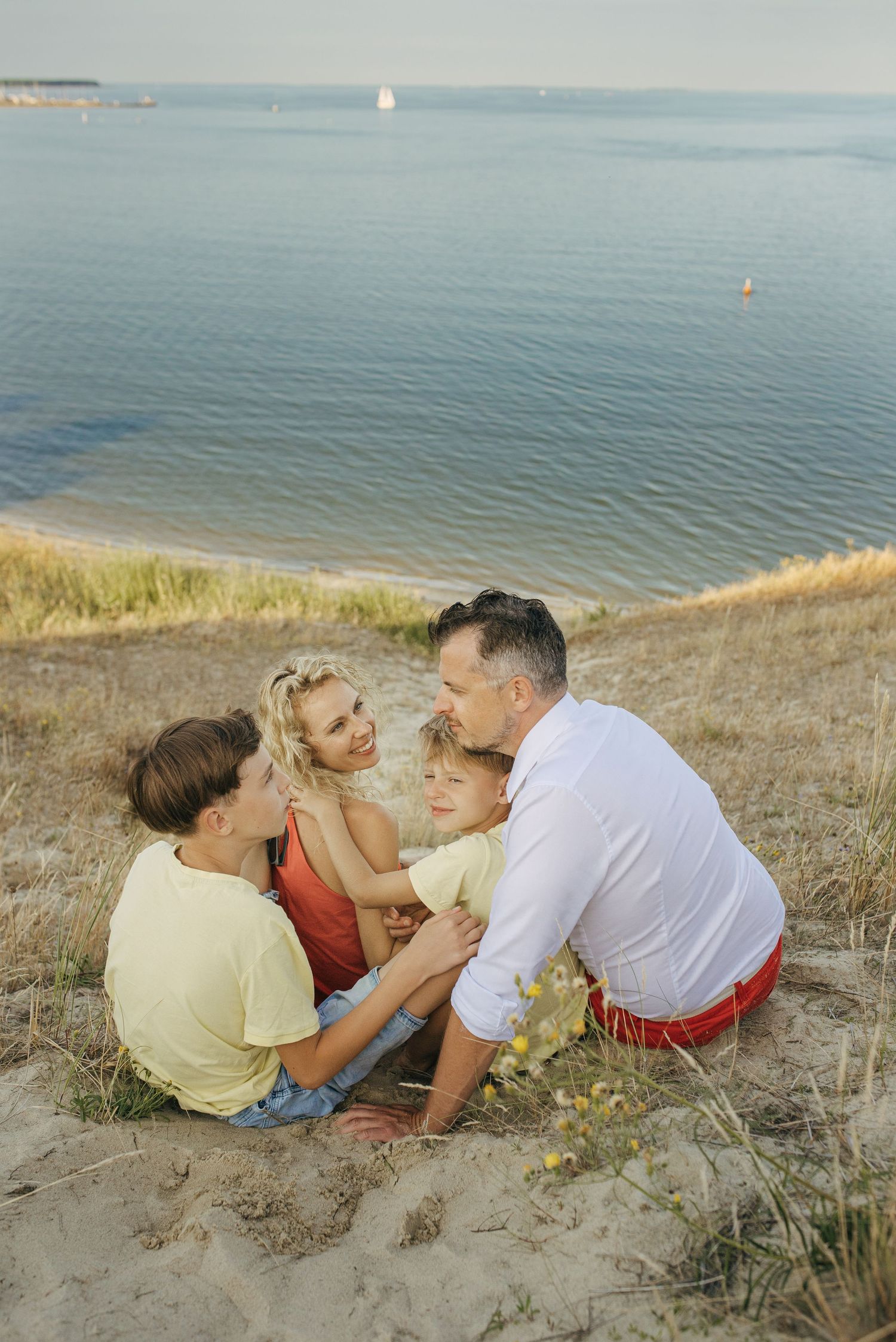 Family relaxing together on a grassy coastal hillside overlooking calm waters.