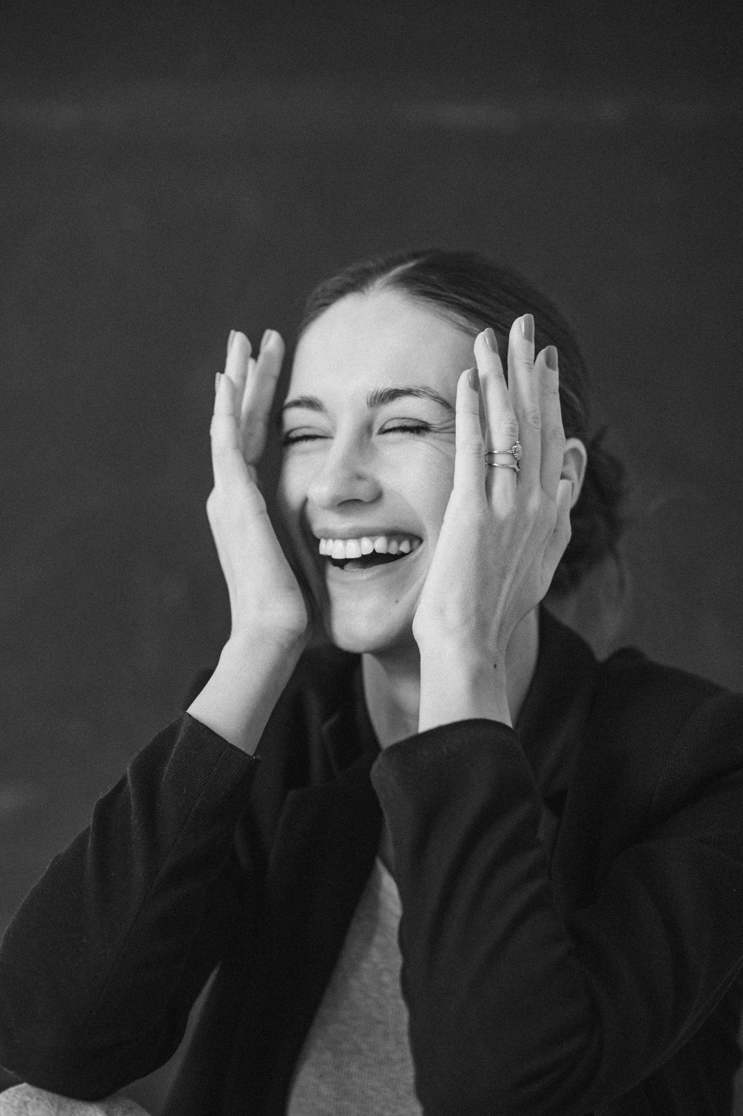 Black and white portrait of person laughing with hands covering face.