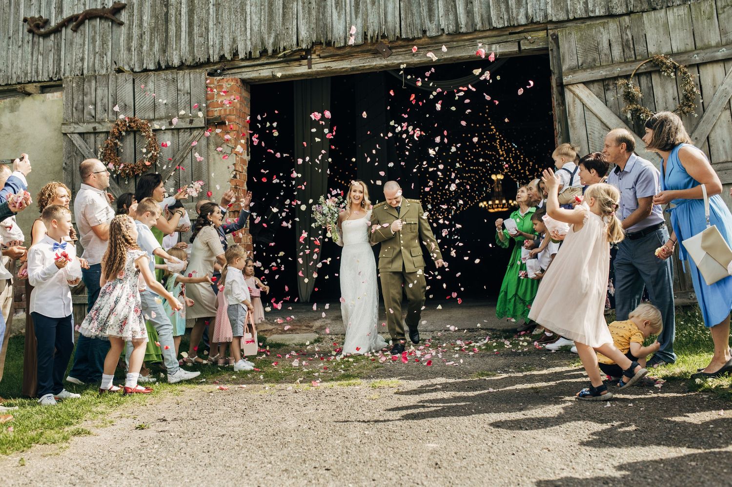 Wedding guests throwing confetti outside a rustic barn during daytime celebration.