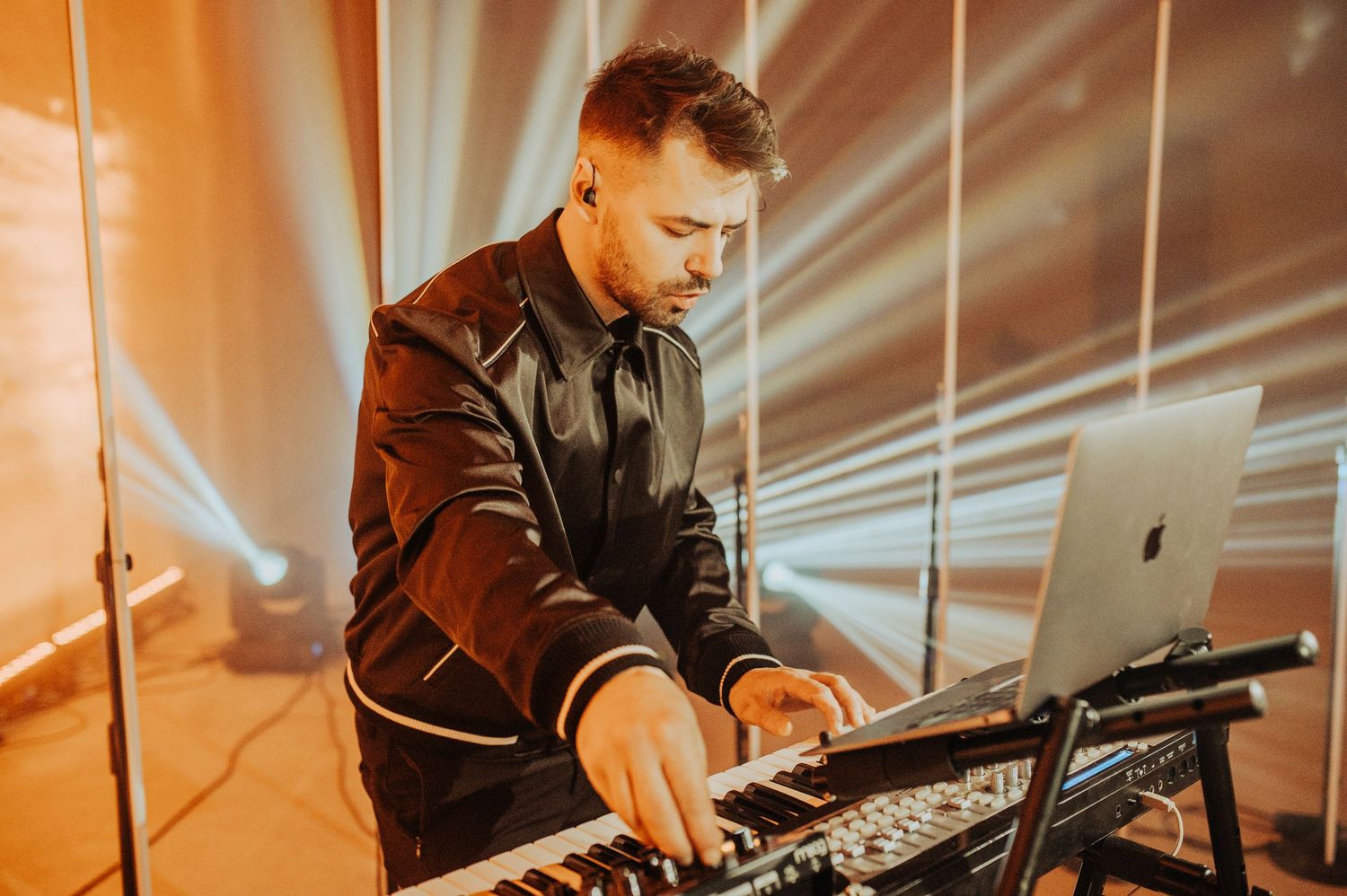 DJ performing at an event with professional lighting equipment and a laptop setup on stage.