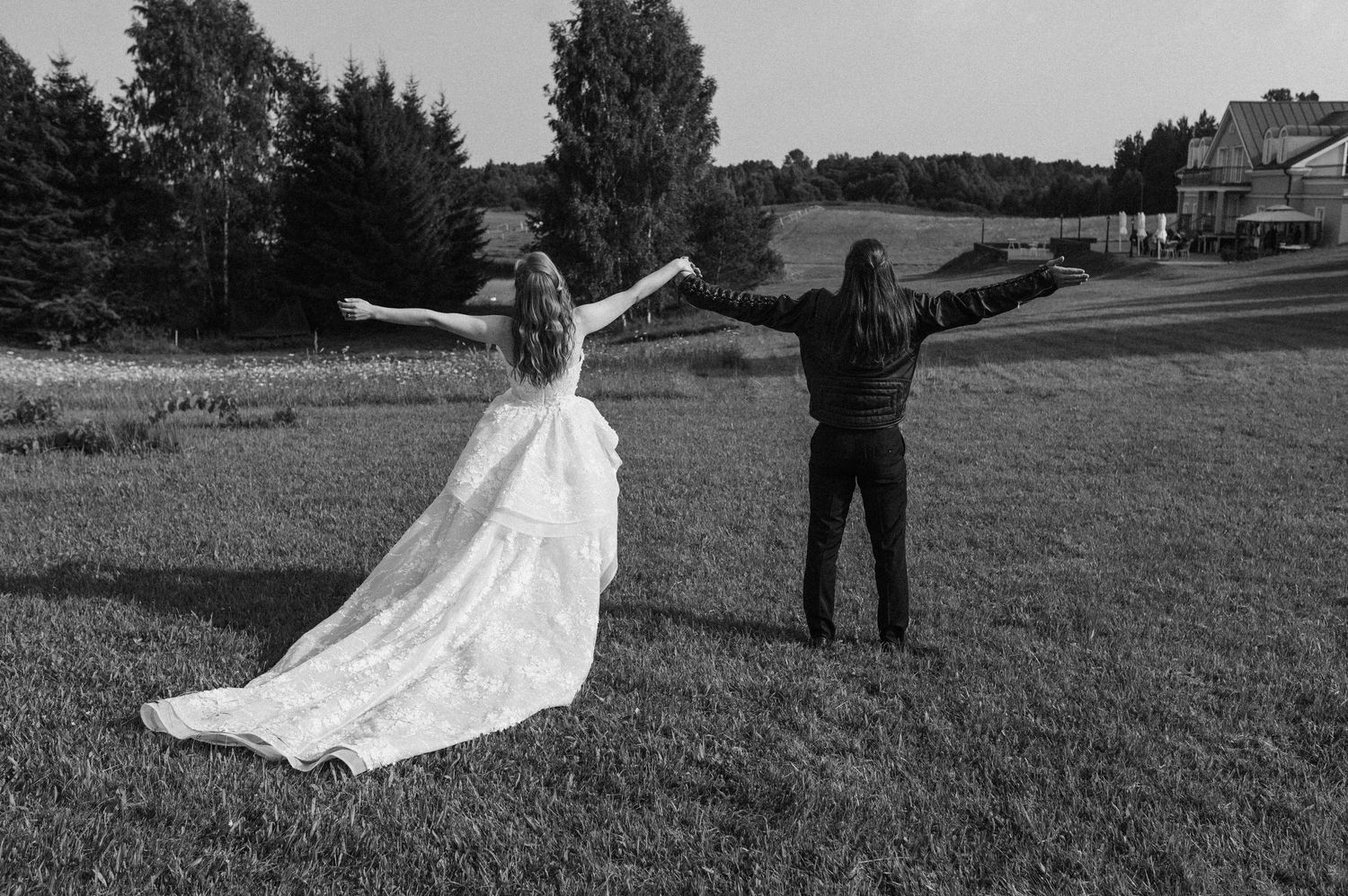 Black and white photo of bride and groom standing in field with arms outstretched on their wedding day.