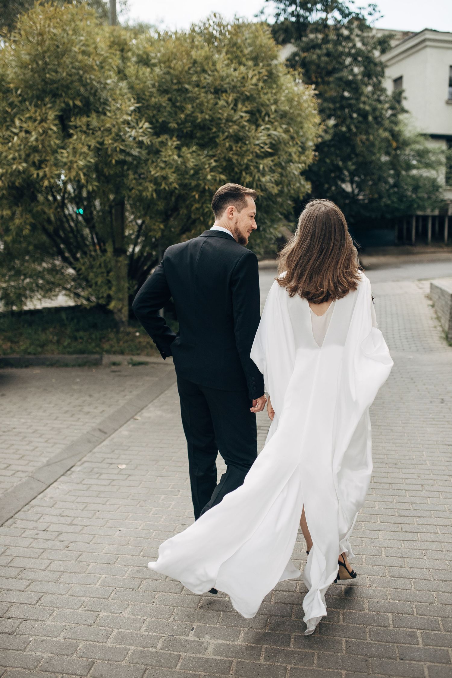 Couple walking together on stone pavement with flowing white dress in motion.