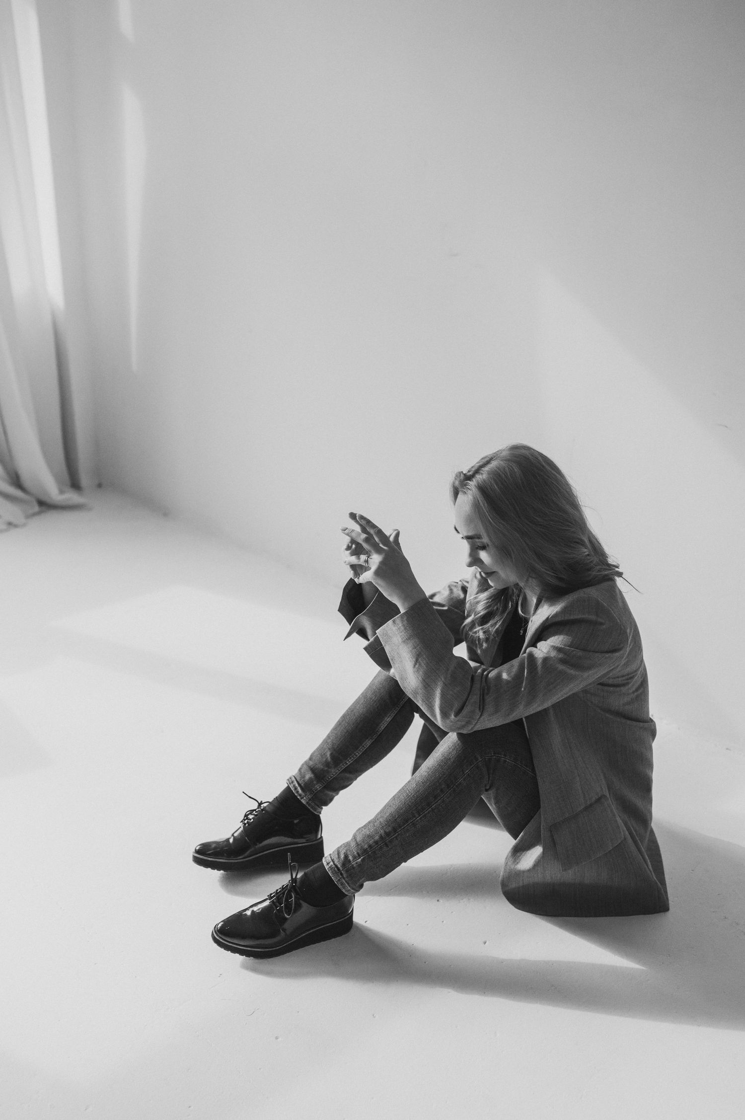Black and white portrait of person sitting against white wall in contemplative poses.
