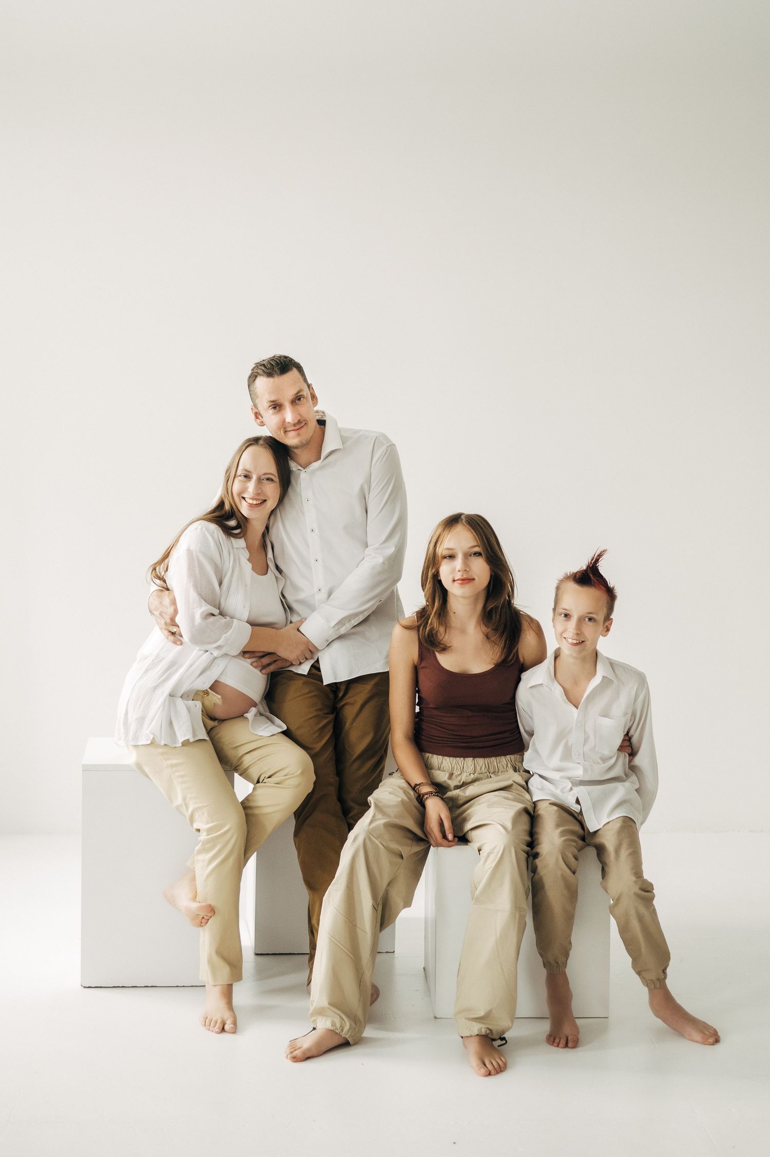 Family sitting together on white bench in coordinated neutral outfits.