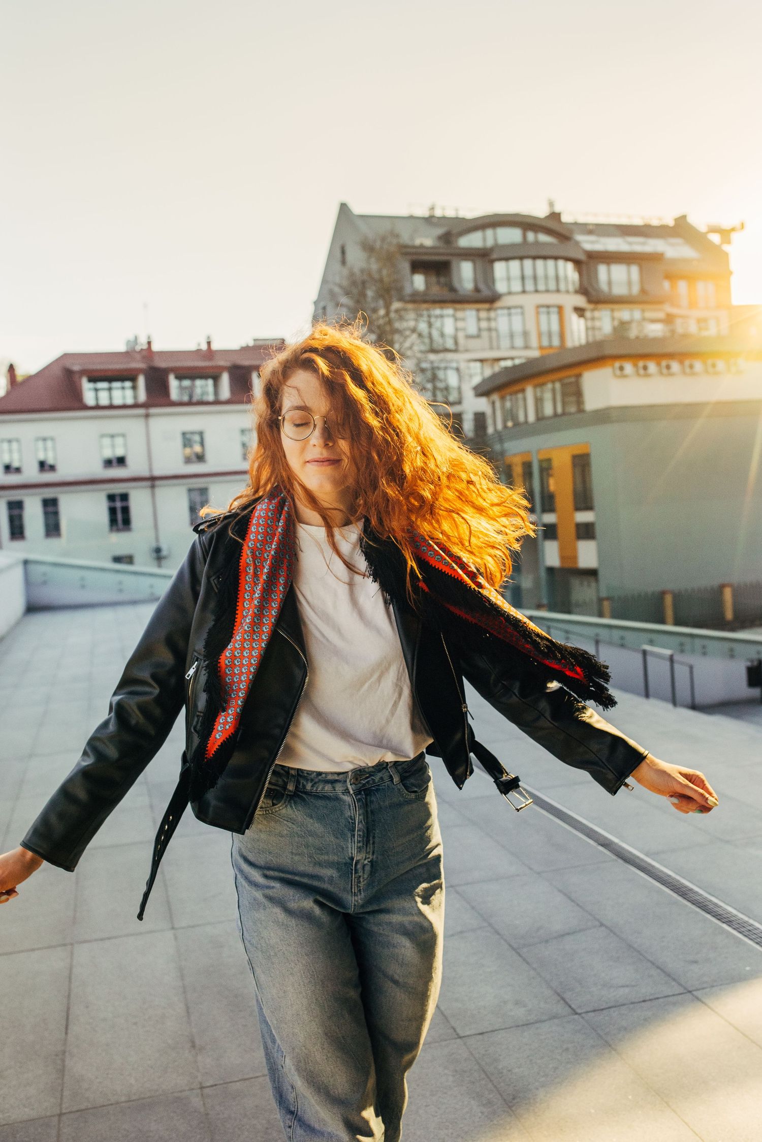Woman in leather jacket dancing energetically on rooftop during golden hour sunset.