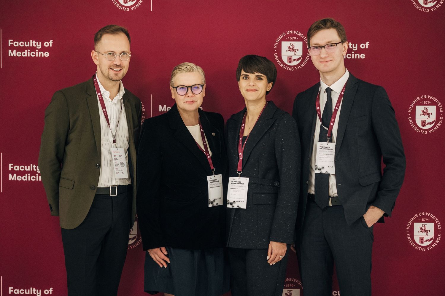 A group of people in formal attire stand together against a burgundy backdrop at a professional event.