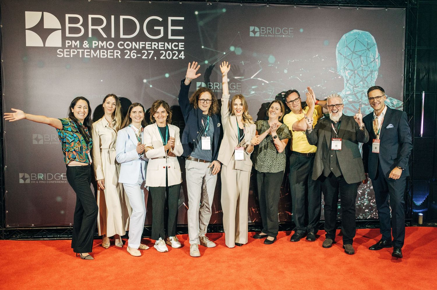 Conference attendees posing for group photos at Bridge event with branded backdrop.