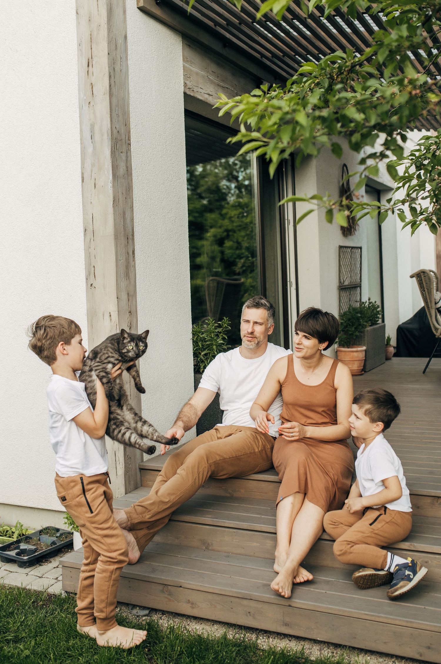 Family relaxing together on a wooden deck porch with a cat.