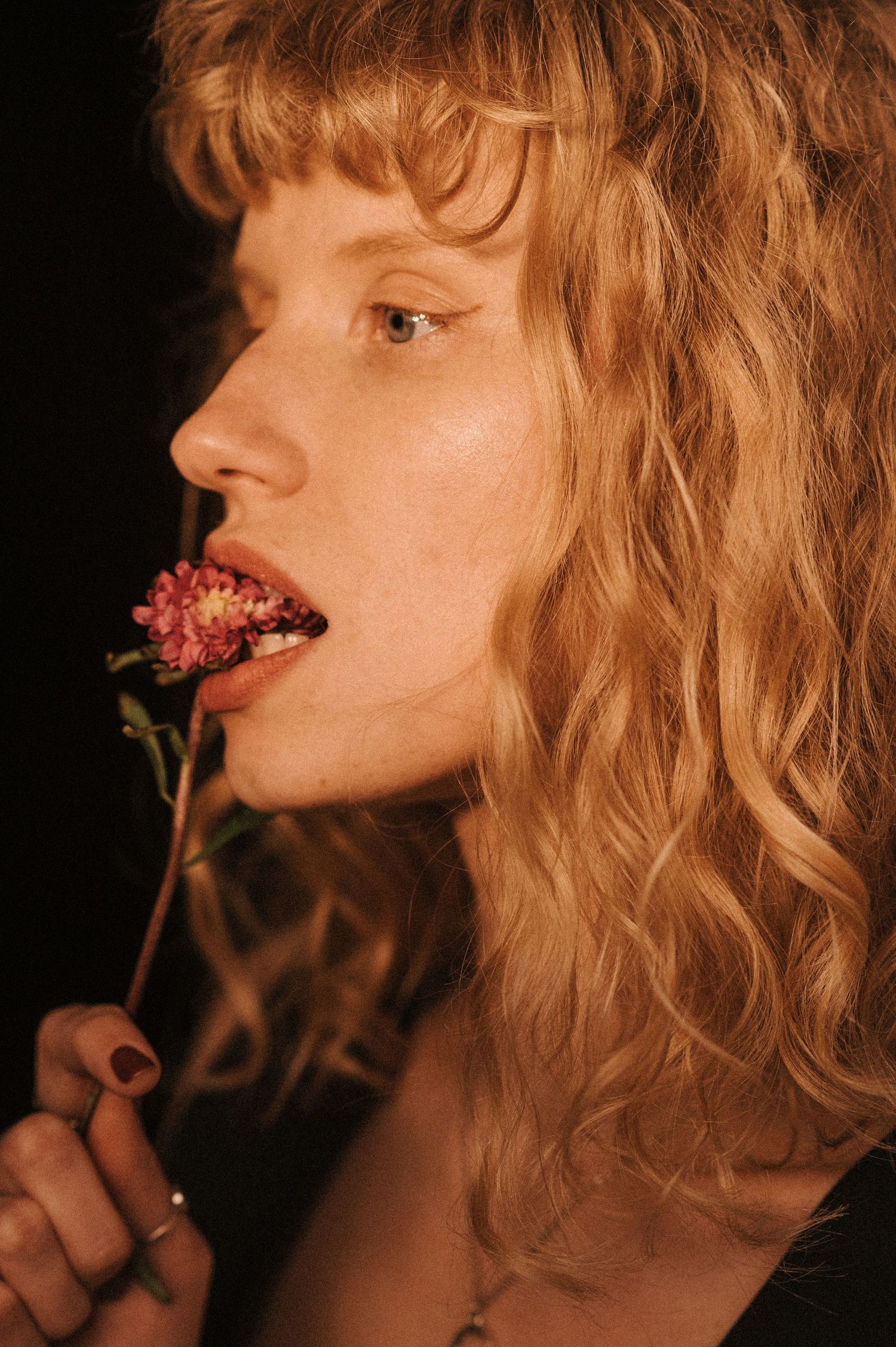 Artistic side profile portrait showing model with flower against dark background.