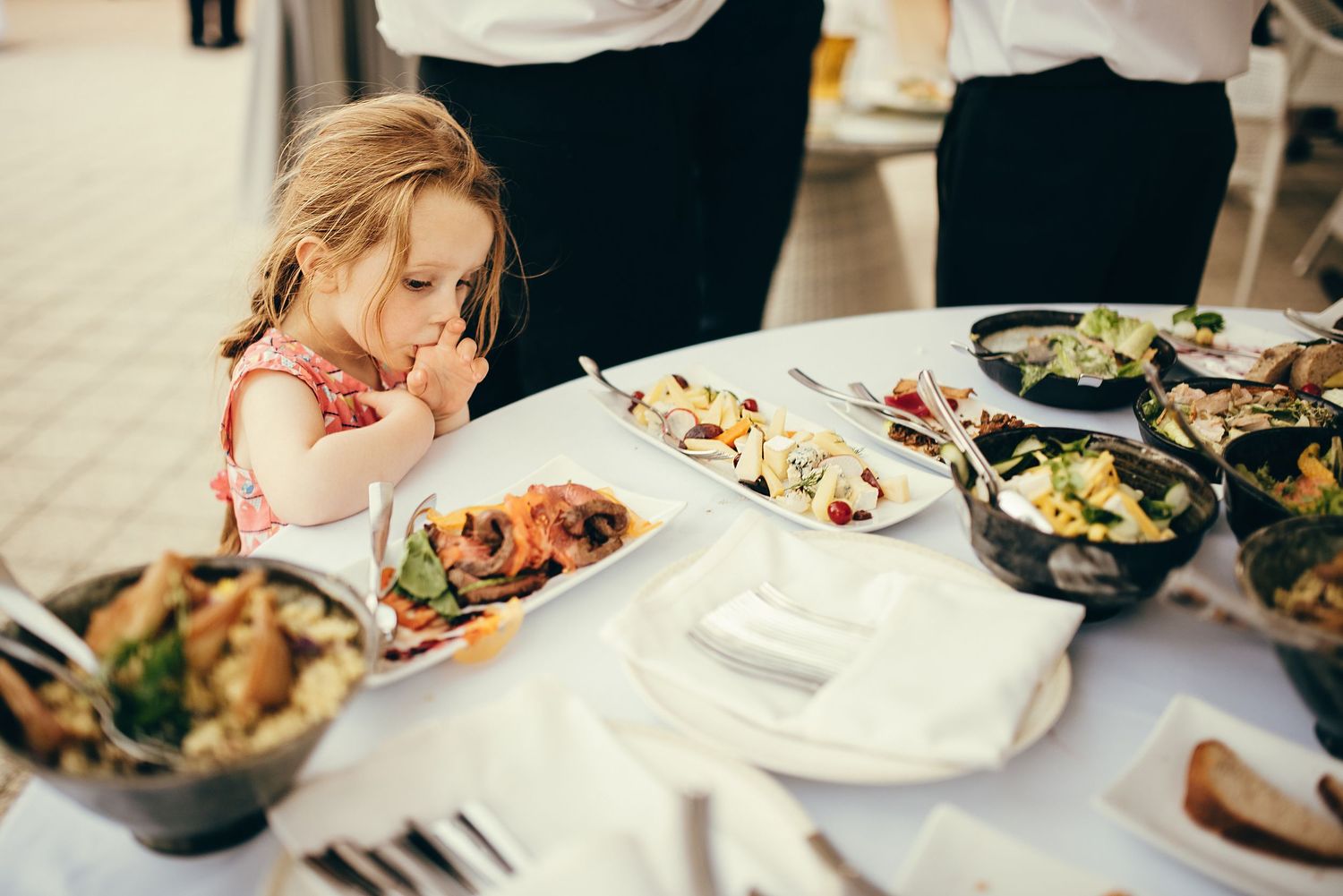 Young girl sampling food at an elegant buffet table filled with various dishes at a restaurant.
