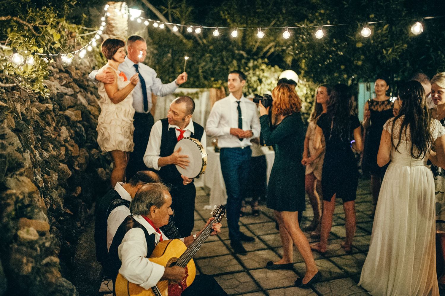 Outdoor evening wedding reception with string lights and dancing guests.