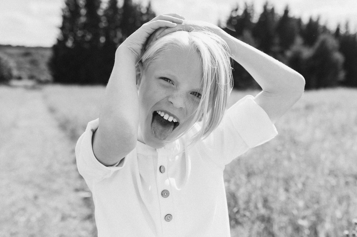 Joyful blonde girl laughing with hands in hair in a black and white outdoor portrait.