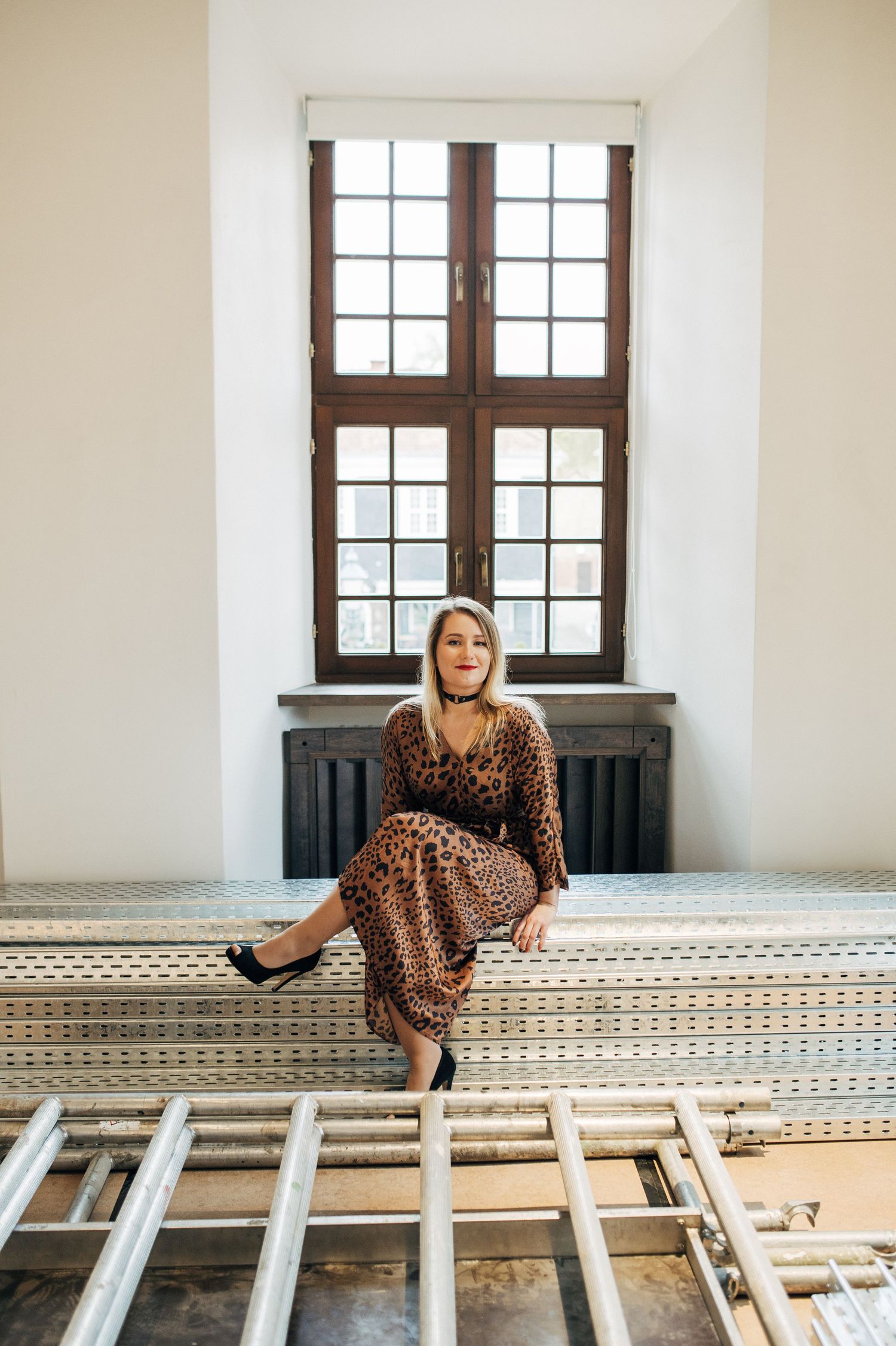 Woman in leopard print dress sitting elegantly by vintage windows.