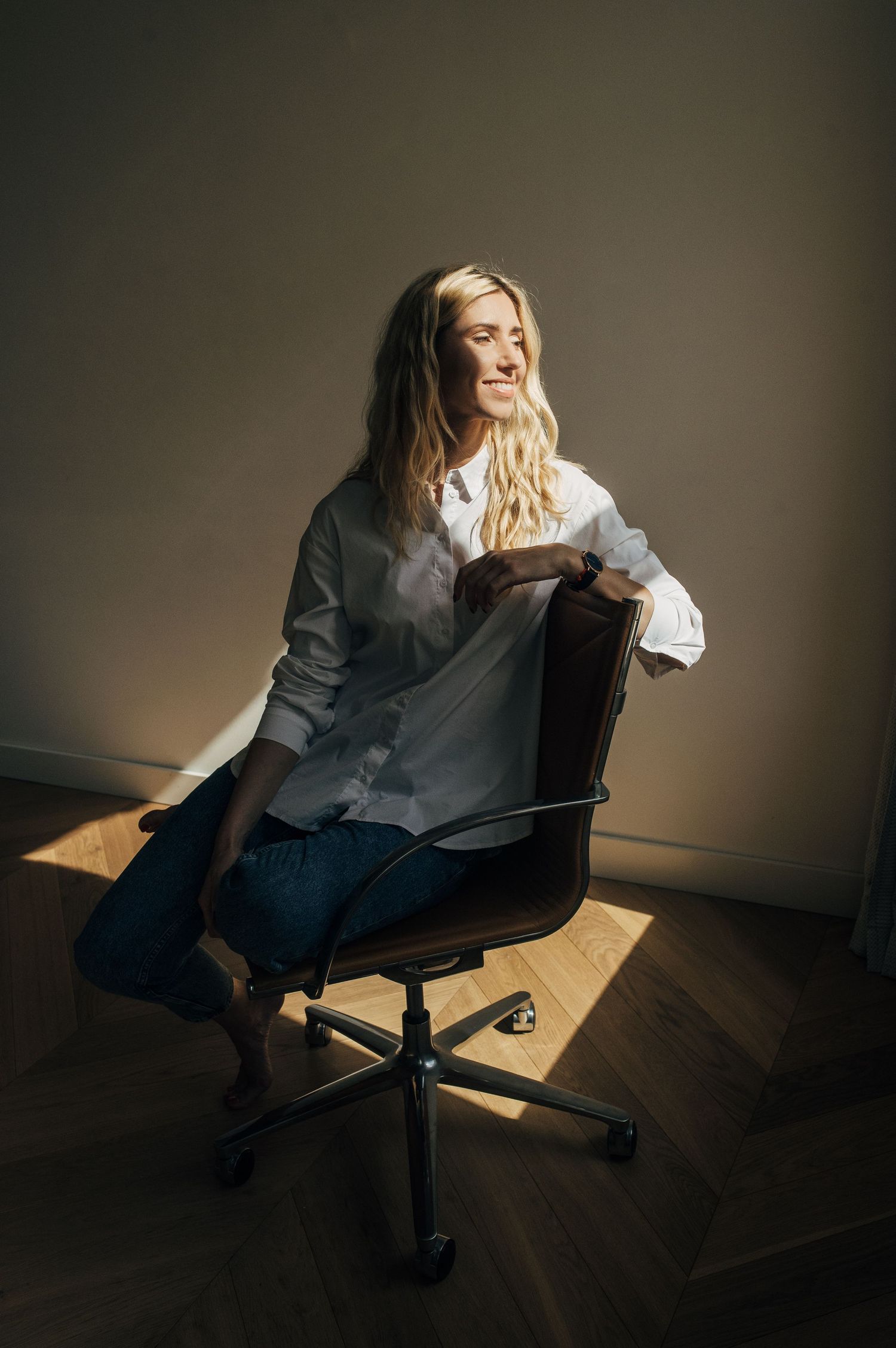 Professional portrait session in dramatic lighting showing a relaxed pose on an office chair.