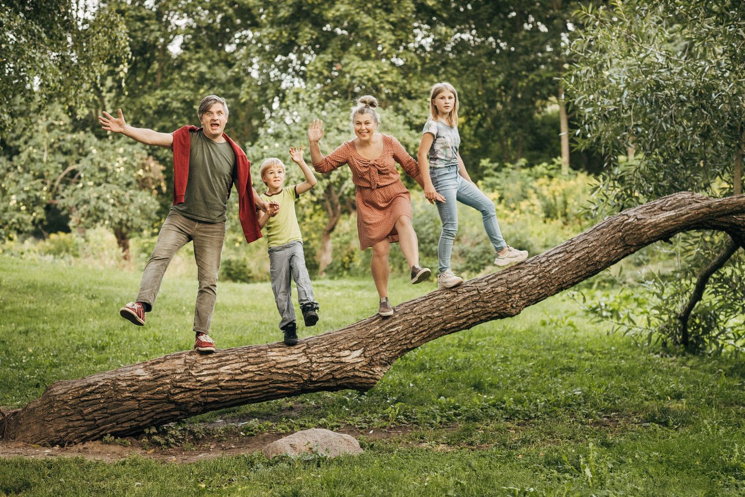 Children playing and climbing on a large fallen tree trunk in a lush green park.