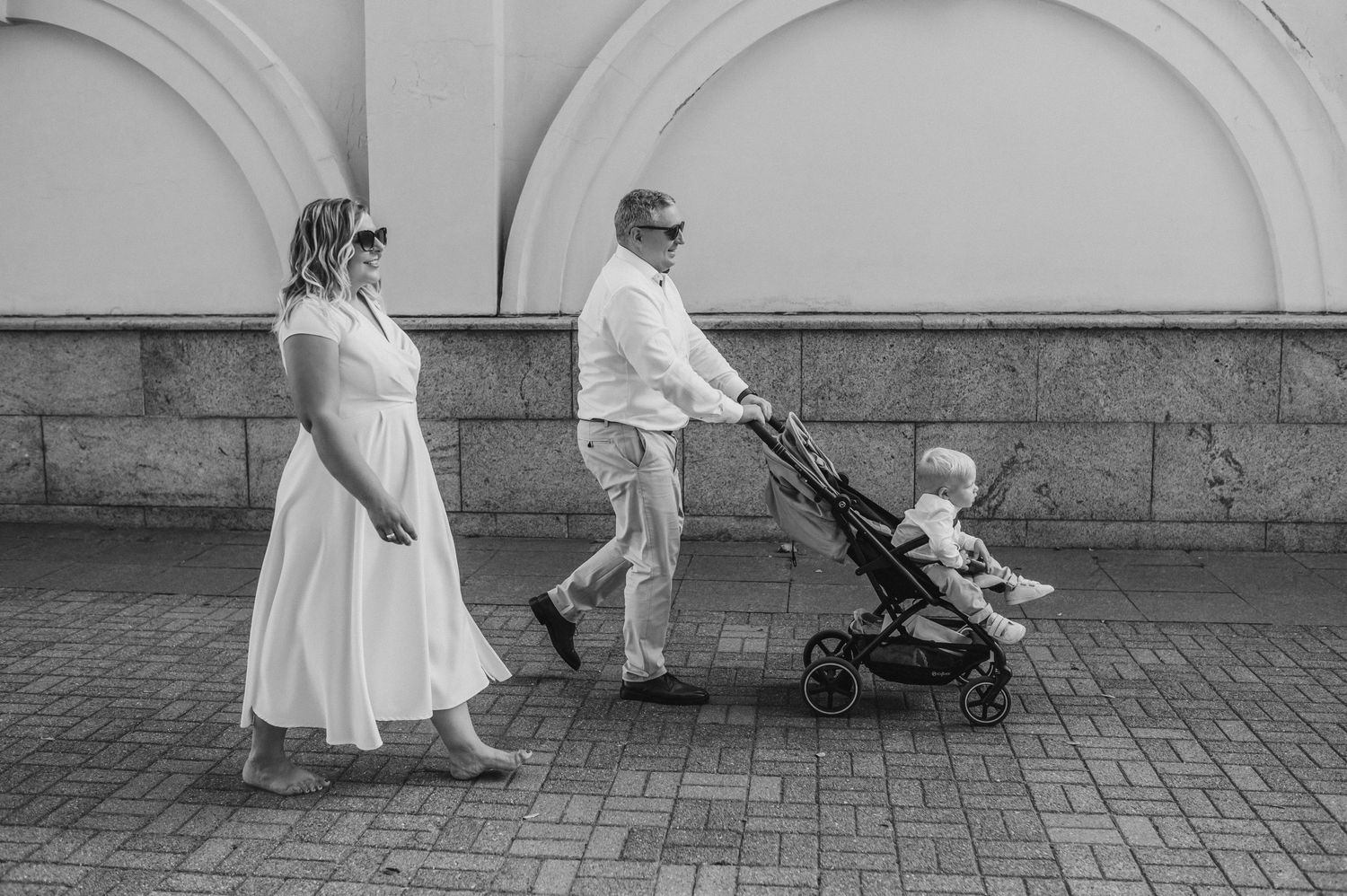 People in white dresses walk along a stone wall creating an elegant composition.