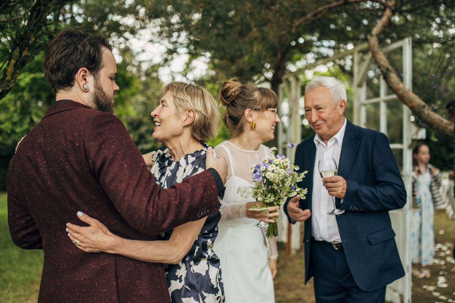 Wedding party celebrating with joyful embraces in a garden setting.