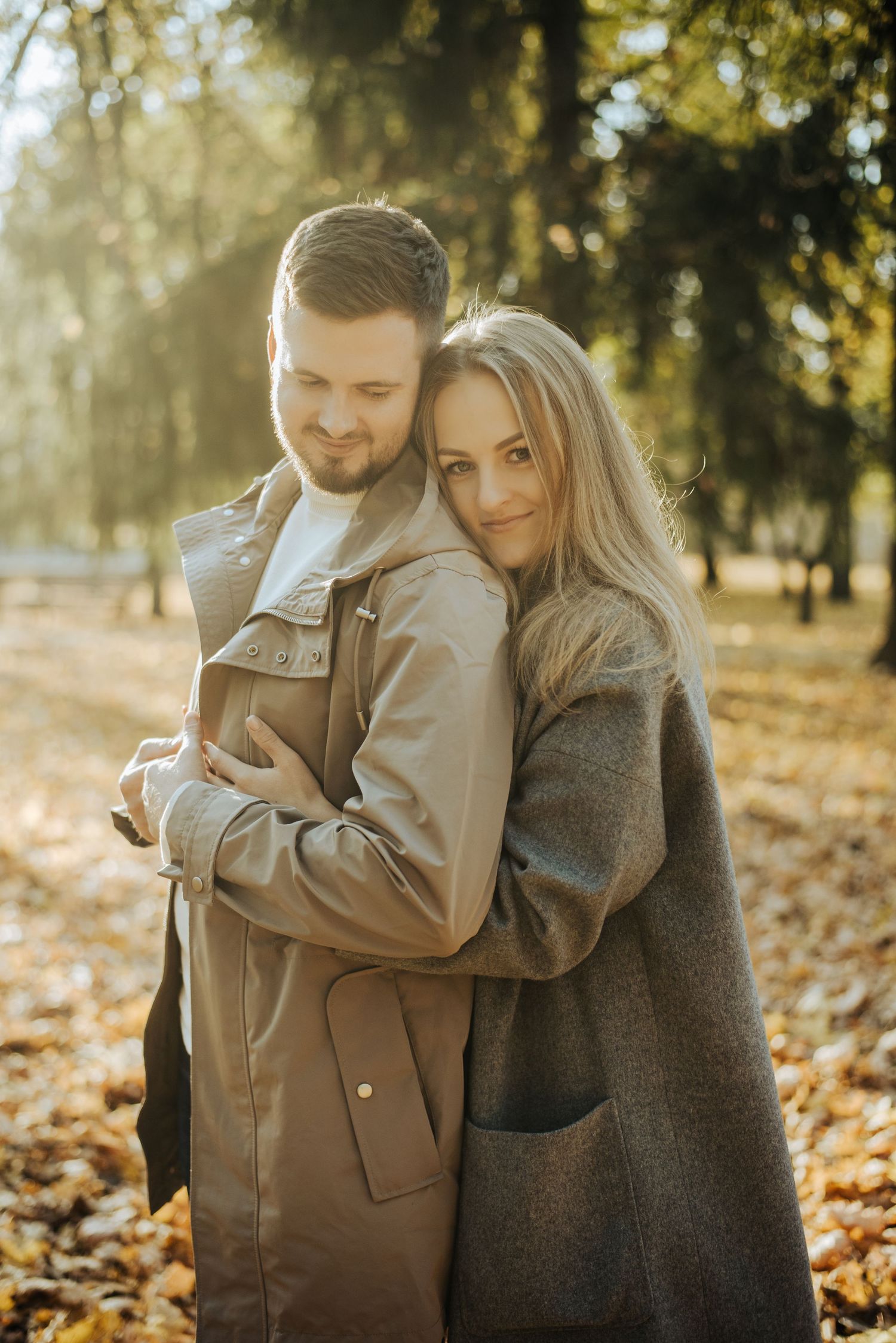 Couple embracing in autumn park with golden sunlight filtering through trees.