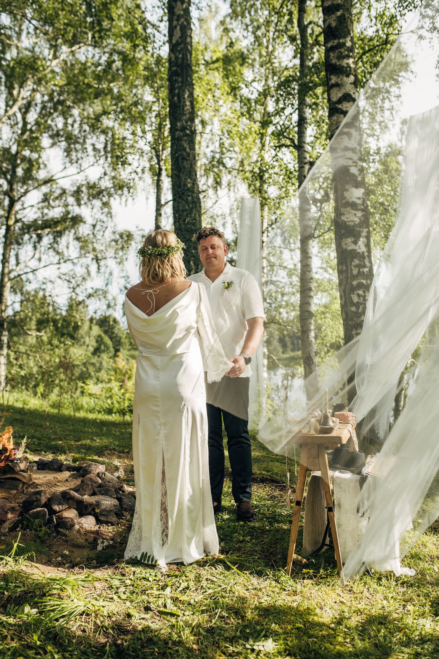A romantic outdoor wedding scene in a sunlit forest with flowing white veils and natural decor.