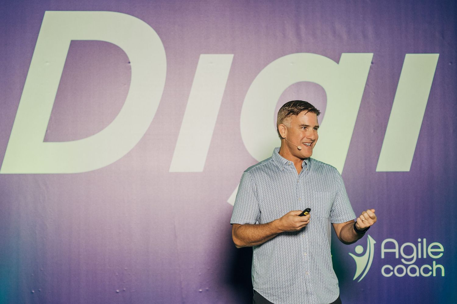A speaker in a light blue shirt presents in front of a large purple wall with 
