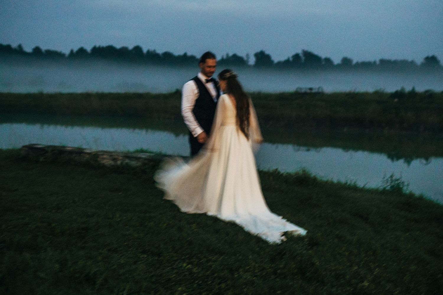 Silhouettes of a wedding couple pose along a lakeside at twilight creating a romantic atmosphere.