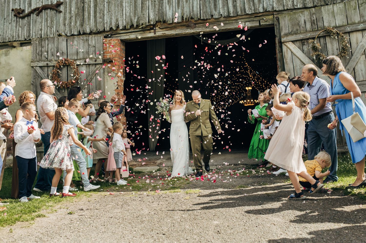 Wedding guests throw pink confetti outside a rustic barn during a celebration.