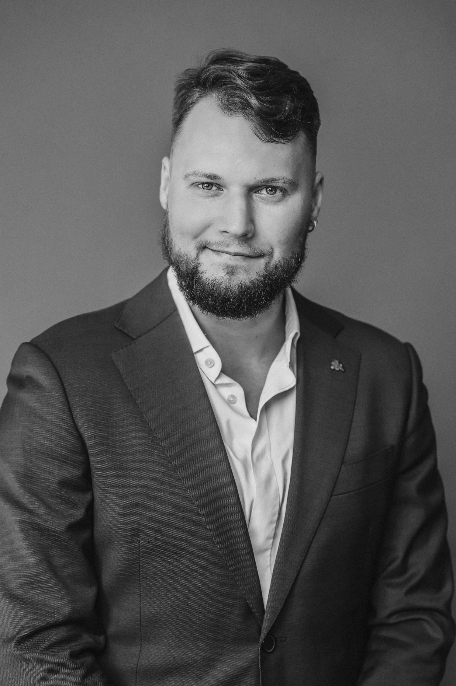 Professional headshot of bearded person in suit jacket and white shirt.