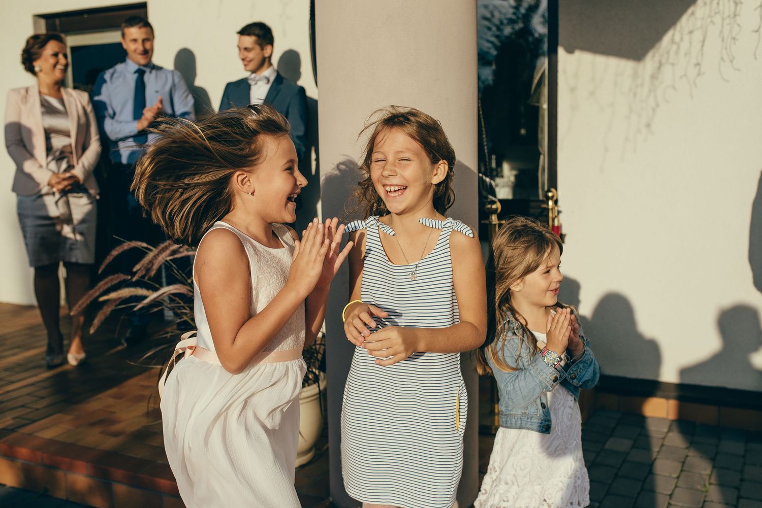 Three joyful girls in dresses laughing and dancing outdoors at a wedding celebration.