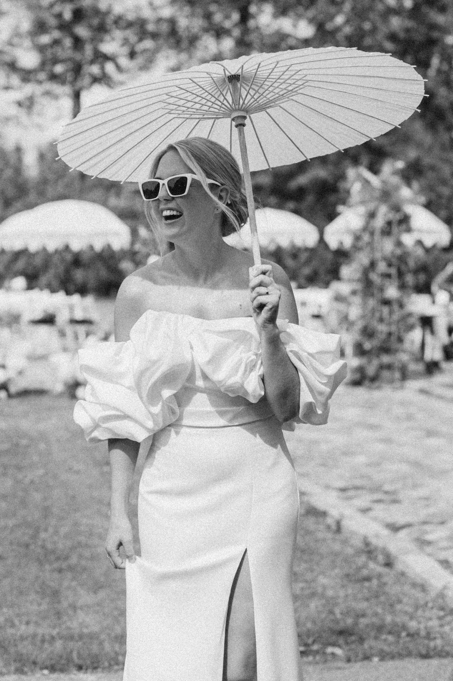 Wedding party holding white parasols outdoors in a stylish black and white photo.