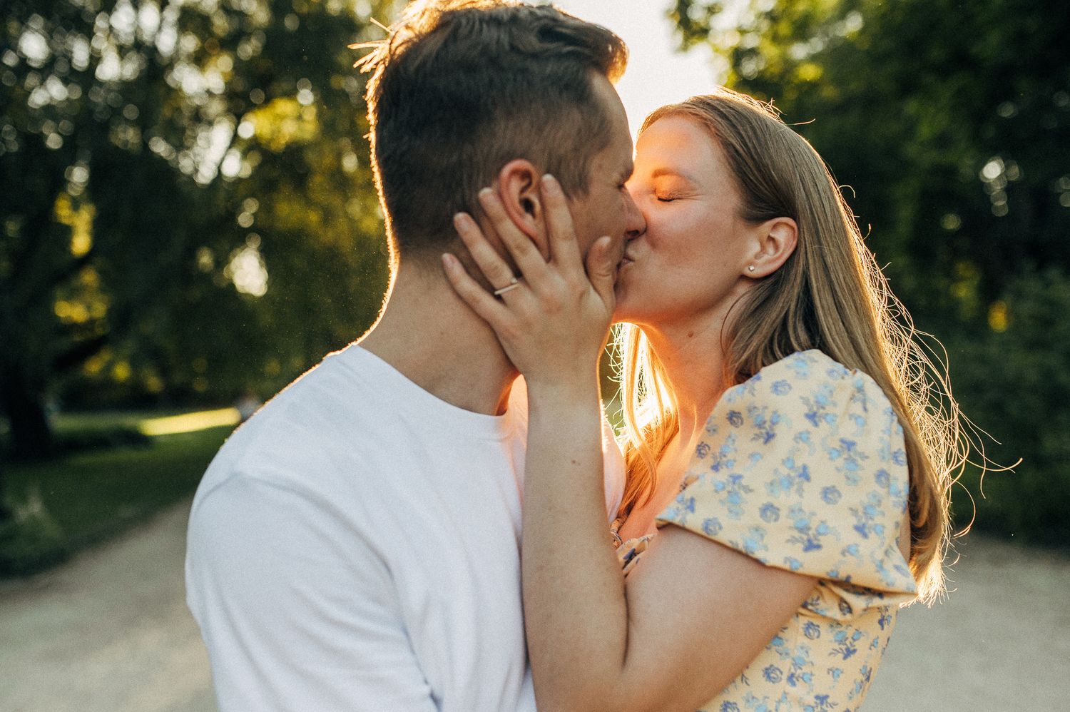 A tender sunset portrait of a couple sharing a kiss in a park with golden backlighting.