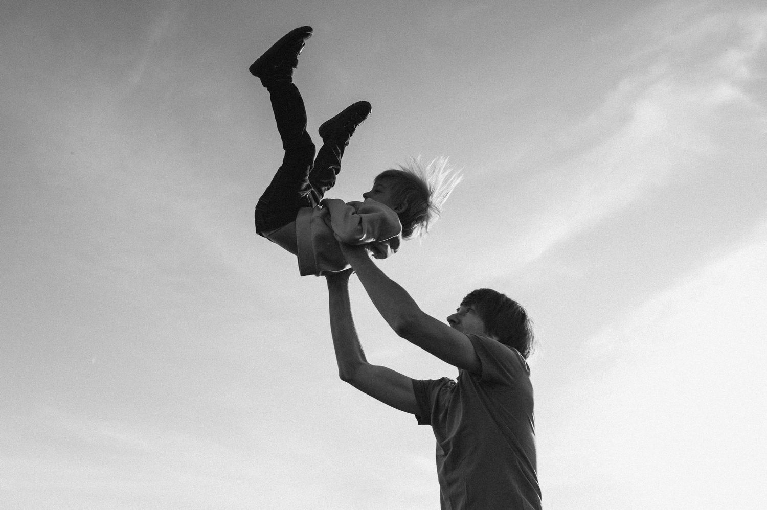 Black and white sequence of silhouettes jumping and playing against bright sky.