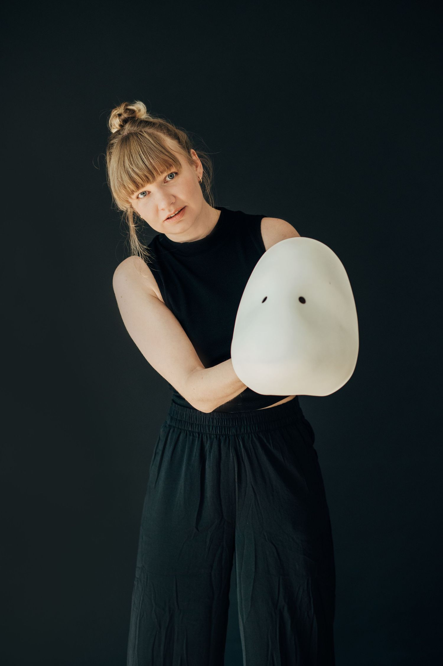 Person in black dress holds and interacts playfully with a white balloon against dark background in artistic portrait series.