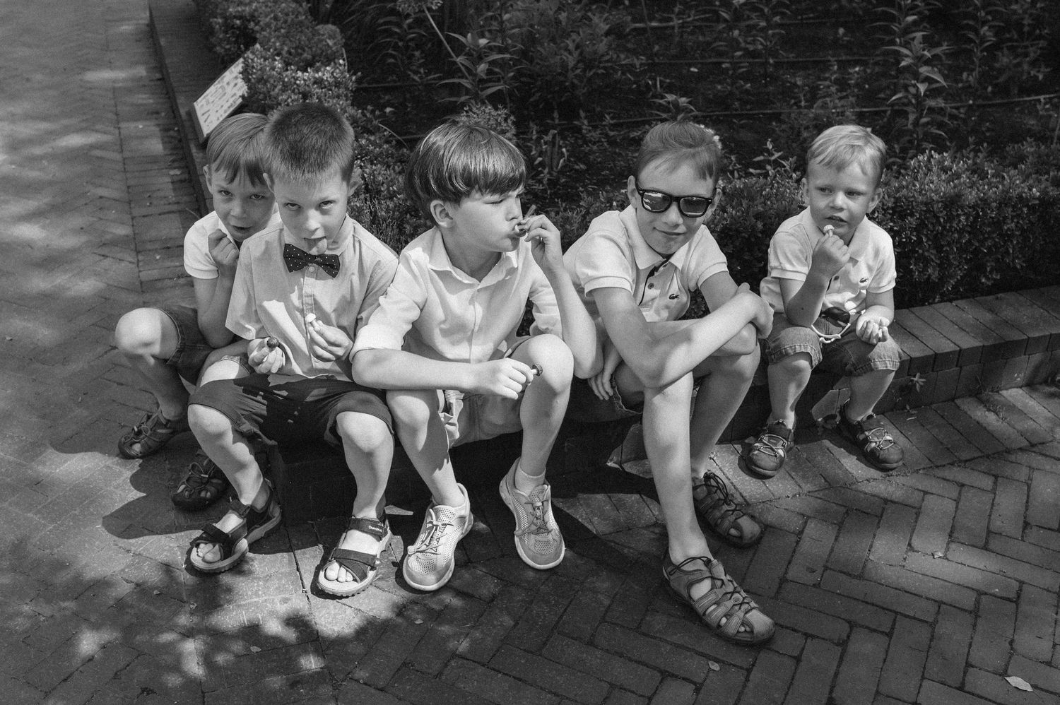 Man and four young boys sitting on a curb eating ice cream in black and white photo.