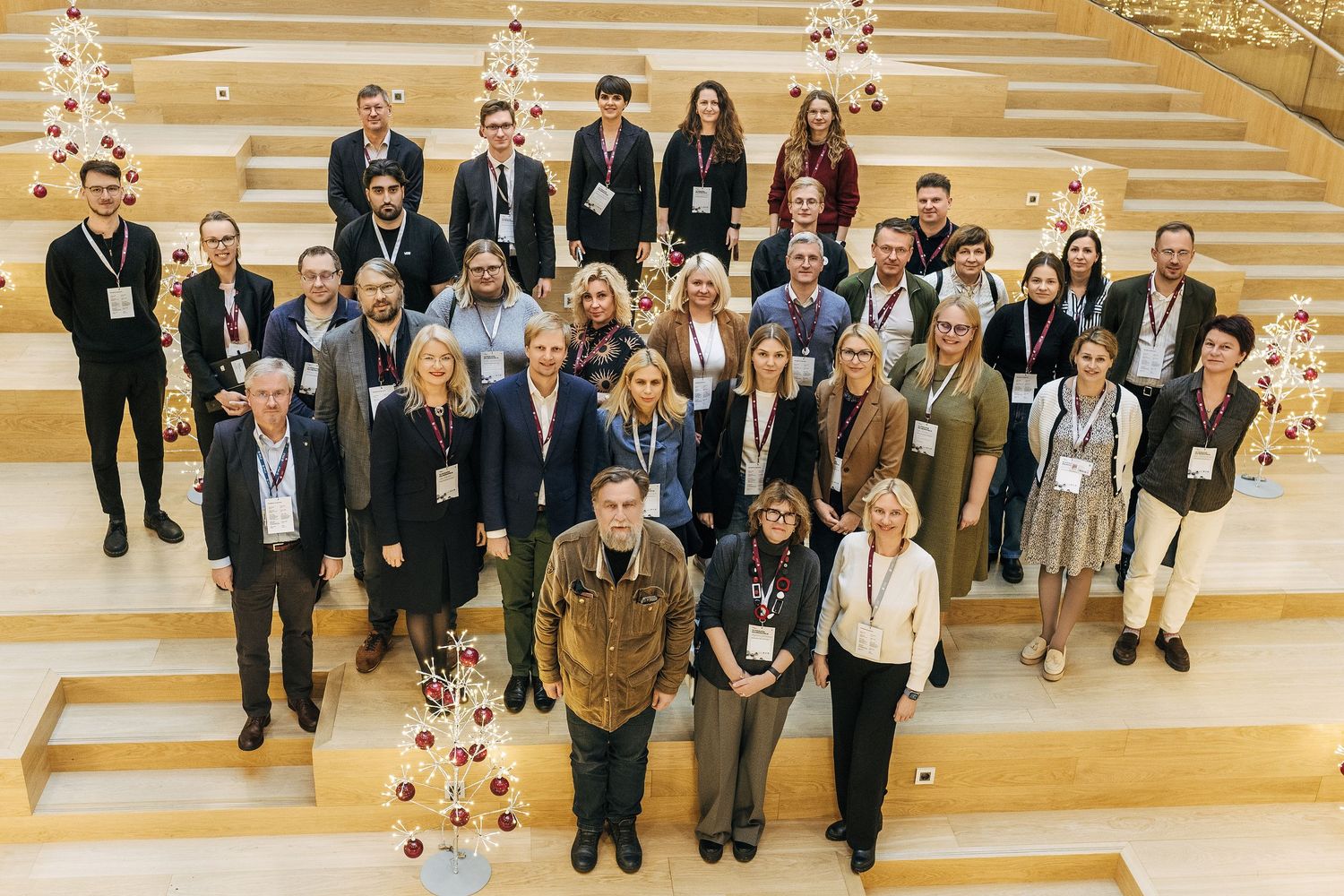 Large group of conference attendees gather on modern wooden staircase for group photo in bright indoor venue.