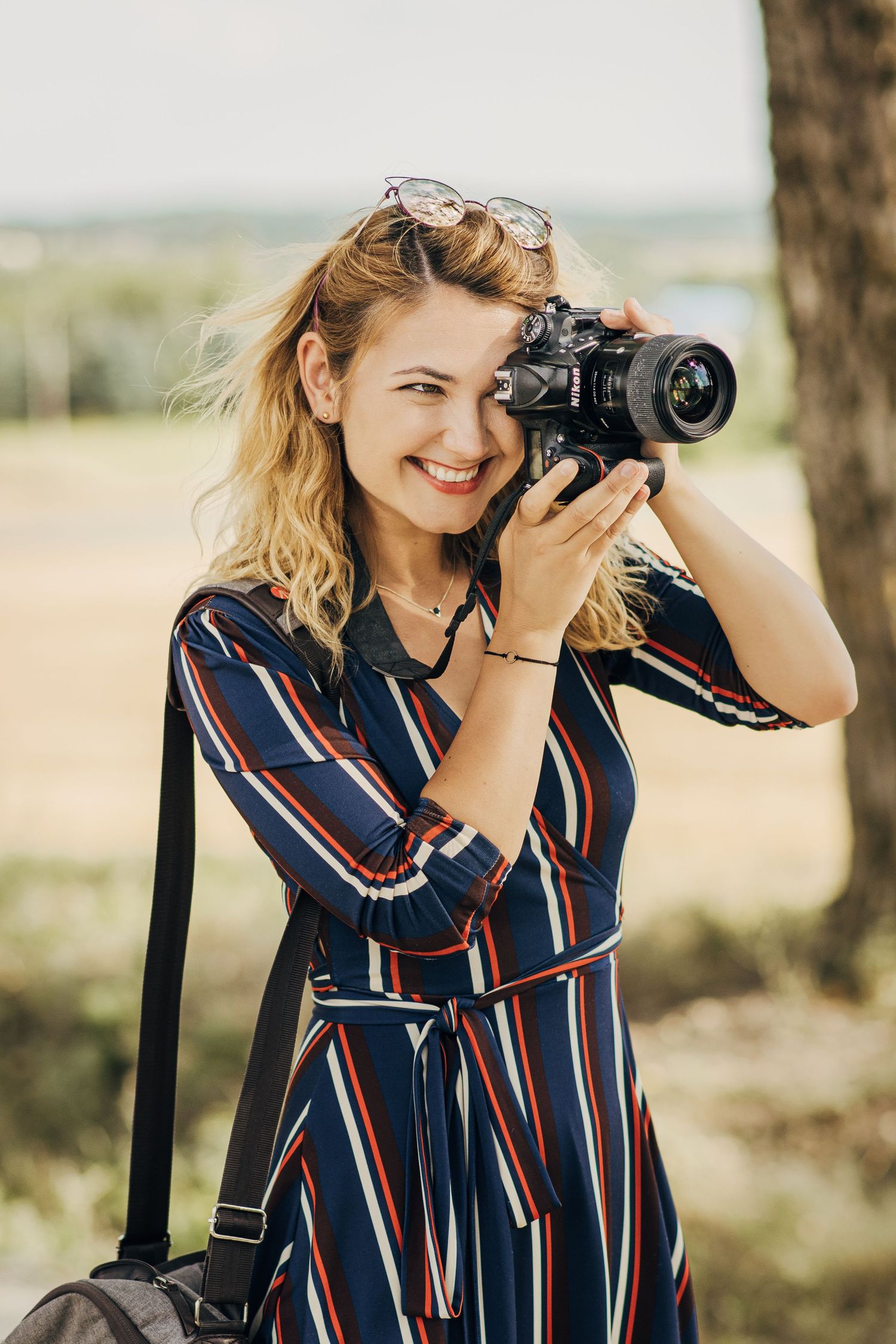 Photographer wearing striped dress taking photos in natural outdoor setting.