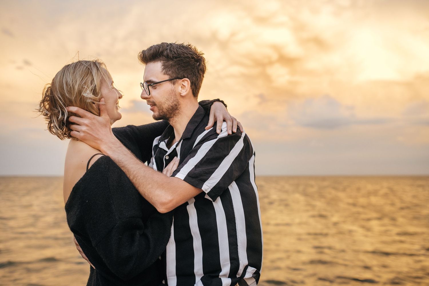 Couple embracing against golden sunset sky over ocean landscape.